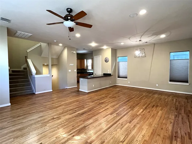 a view of an empty room and kitchen with wooden floor