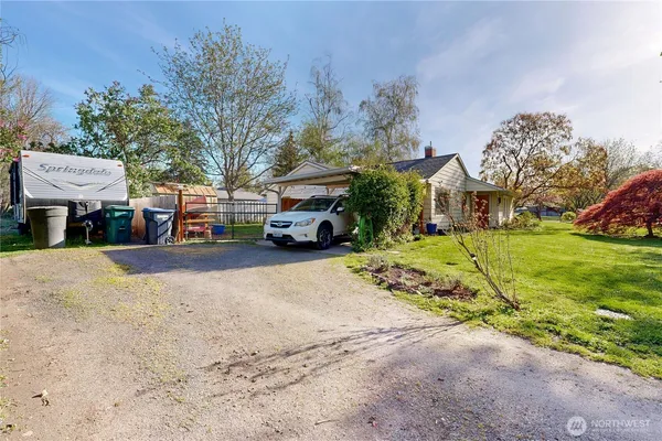 a view of a white house in front of a big yard with plants and large trees