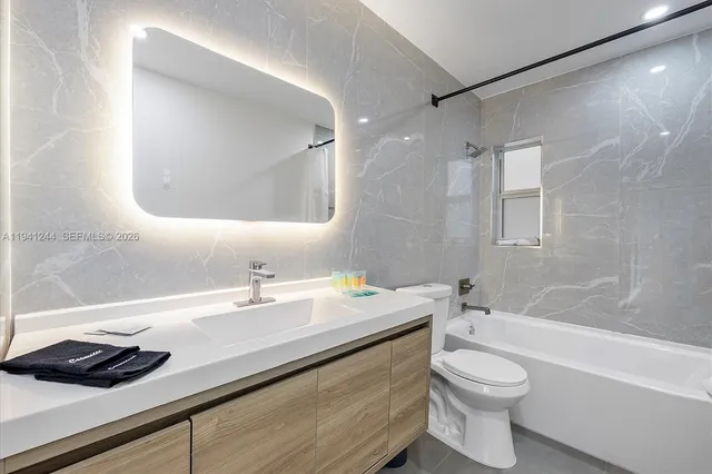 a bathroom with a granite countertop sink a toilet a mirror and bathtub