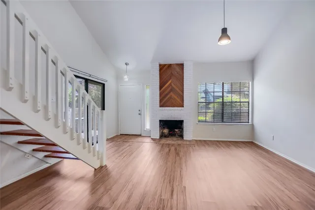 a view of an empty room with wooden floor fireplace and a window