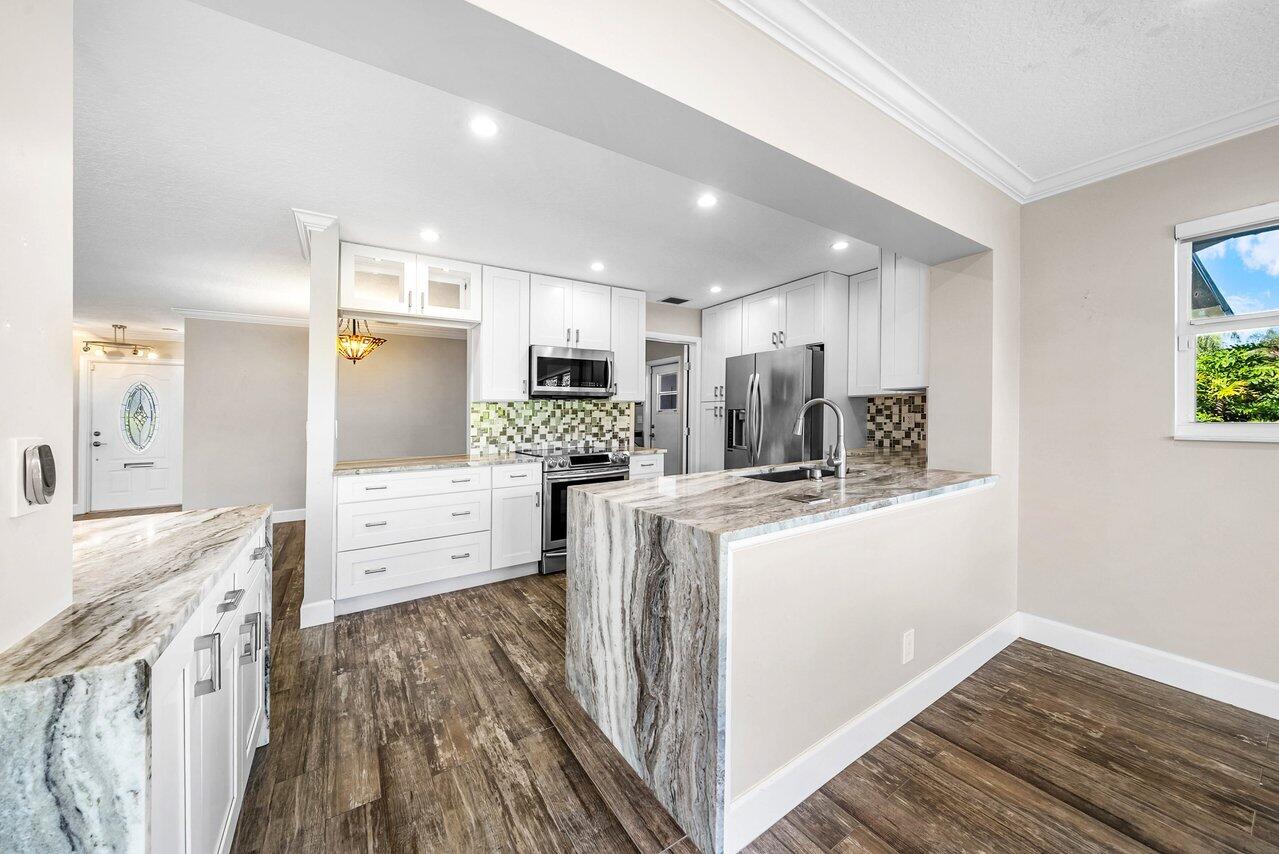 401 French Royale Circle Atlantis, FL 33462 - Photo 16 of 47 a kitchen with kitchen island a sink a stove a refrigerator cabinets and wooden floor