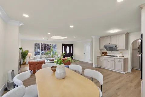 a kitchen with stainless steel appliances kitchen island granite countertop a refrigerator a sink dishwasher a dining table and chairs with wooden floor