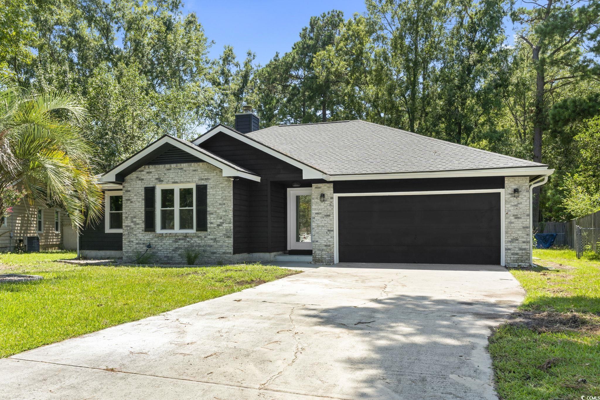 220 Rice Mill Drive Myrtle Beach, SC 29588 - Photo 1 of 31 View of front of home featuring brick siding, driveway, a chimney, an attached garage, and a shingled roof