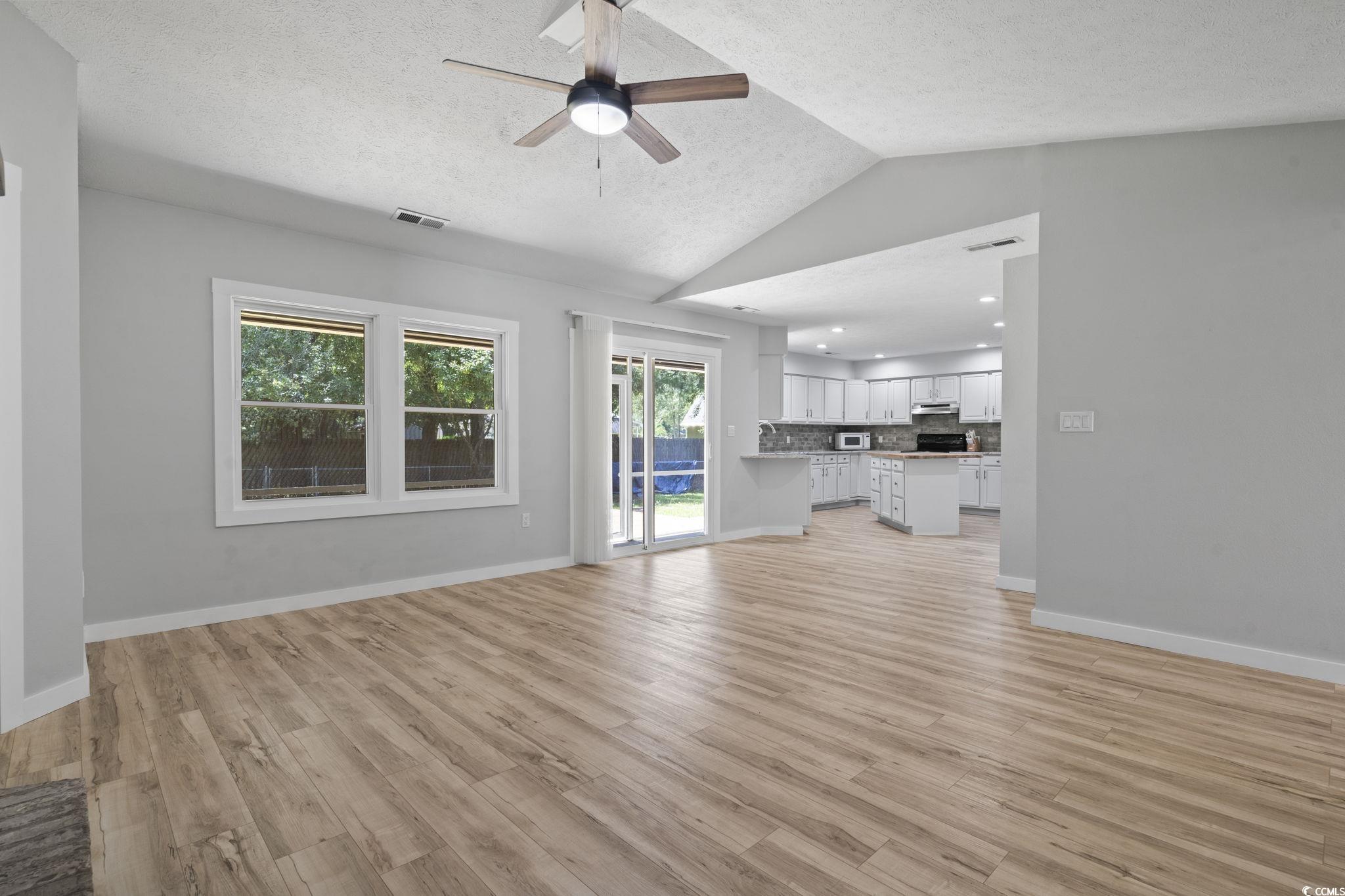 220 Rice Mill Drive Myrtle Beach, SC 29588 - Photo 12 of 31 Unfurnished living room featuring lofted ceiling, a ceiling fan, a textured ceiling, and light wood-type flooring
