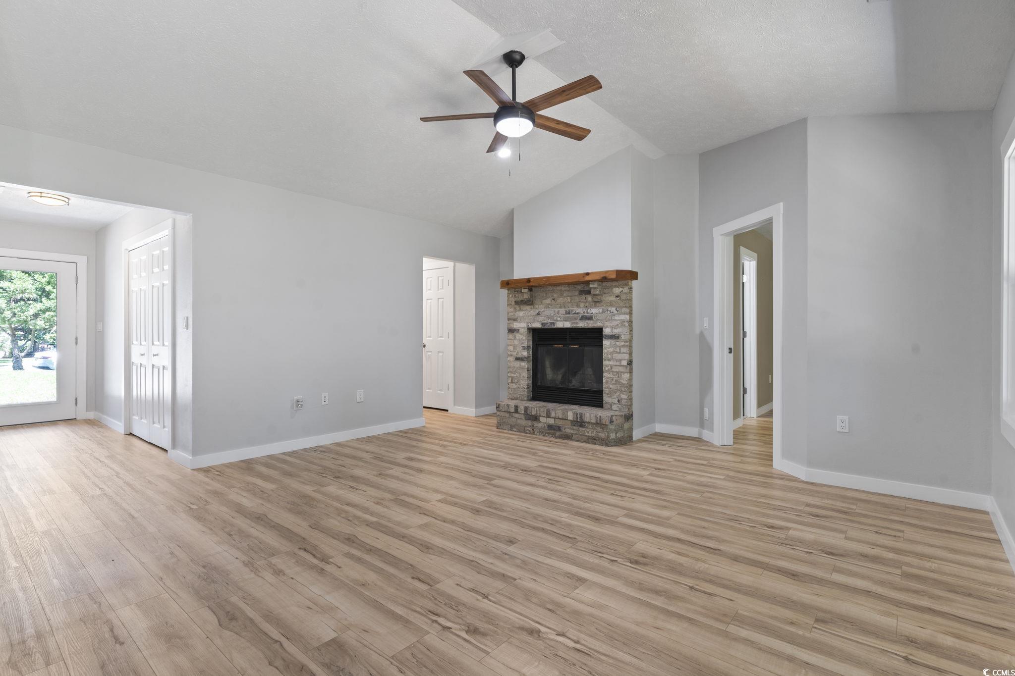 220 Rice Mill Drive Myrtle Beach, SC 29588 - Photo 13 of 31 Unfurnished living room featuring ceiling fan, light wood-style flooring, lofted ceiling, and a fireplace
