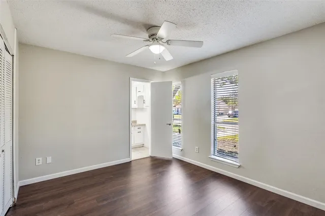 an empty room with wooden floor chandelier fan and windows