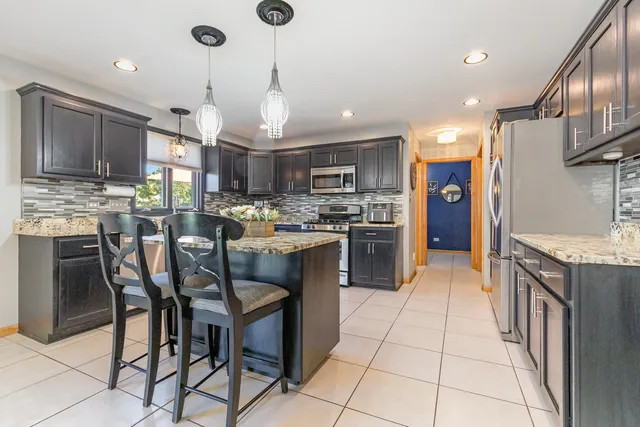 a kitchen with stainless steel appliances granite countertop a stove top oven a refrigerator a sink and a dining table with wooden cabinets