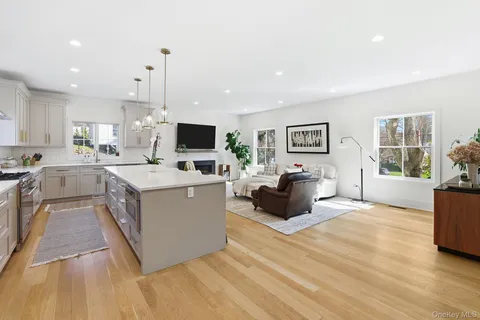 a large white open kitchen with stainless steel appliances kitchen island a stove a sink dishwasher a refrigerator with white cabinets and wooden floor