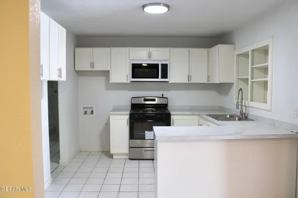 a kitchen with granite countertop a sink a stove top oven and cabinetry