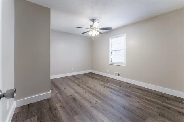 an empty room with wooden floor ceiling fan and window