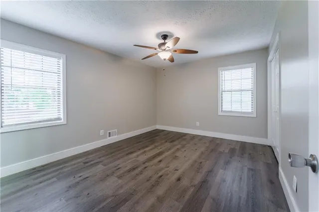 an empty room with wooden floor ceiling fan and windows