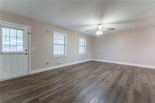an empty room with wooden floor chandelier fan and windows