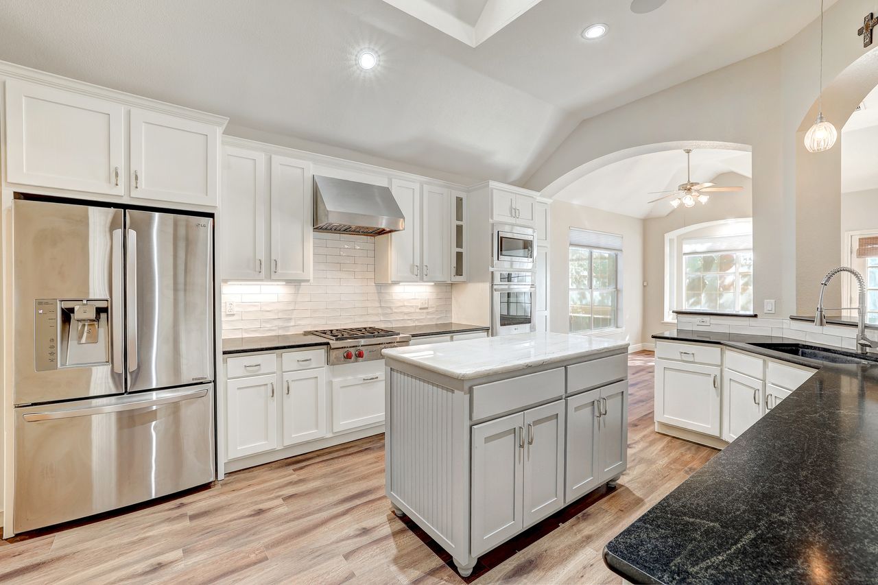 Kitchen featuring appliances with stainless steel finishes, hanging light fixtures, white cabinetry, a ceiling fan, and vaulted ceiling with huge skylight