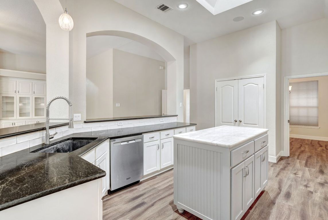 301 Rim Rock Drive Georgetown, TX 78628 - Photo 15 of 40 Kitchen featuring white cabinetry, a kitchen island, hanging light fixtures, stainless steel dishwasher, and dark stone counters