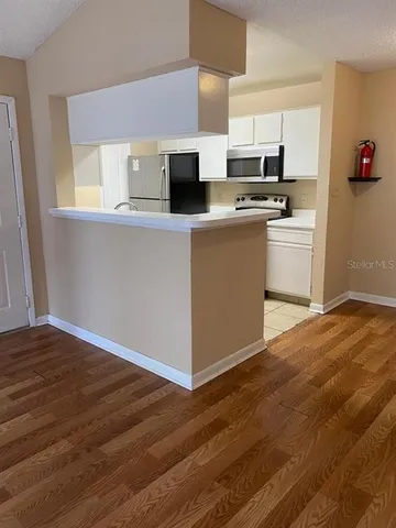 a kitchen with stainless steel appliances a sink dishwasher a stove top oven a refrigerator and white cabinets with wooden floor