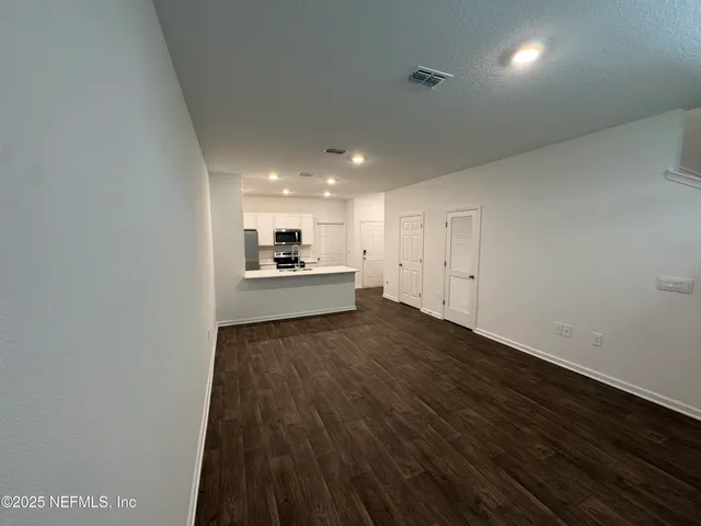 a view of kitchen and empty room with wooden floor
