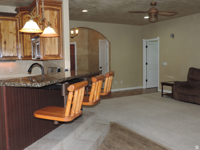 140 North 200 E Street Glenwood, UT 84730 - Photo 6 of 54 Kitchen featuring a breakfast bar, dark stone counters, pendant lighting, ceiling fan, and stainless steel microwave