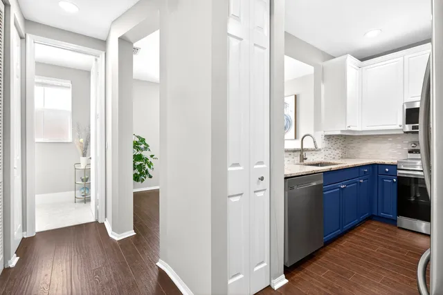 a kitchen with stainless steel appliances granite countertop a refrigerator a sink and white cabinets with wooden floor