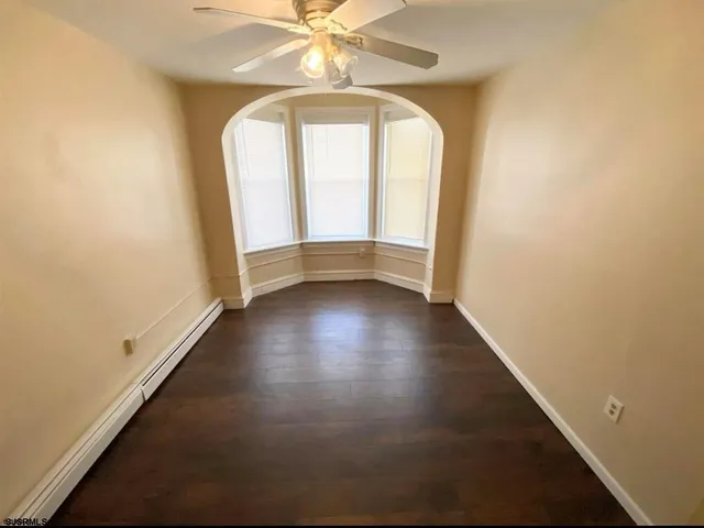 an empty room with wooden floor fan and windows
