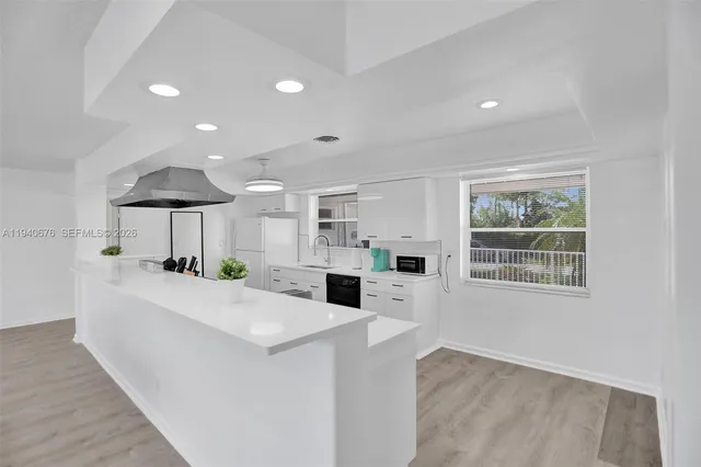a large white kitchen with kitchen island a stove a sink a refrigerator and white cabinets with wooden floor