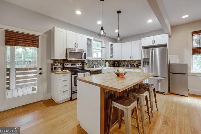 a kitchen with granite countertop a stove a sink a kitchen island with stainless steel appliances cabinets and wooden floor