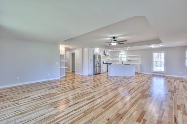a view of an empty room with wooden floor and a kitchen view