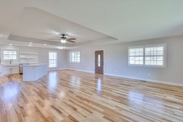 a view of an empty room with wooden floor and a kitchen
