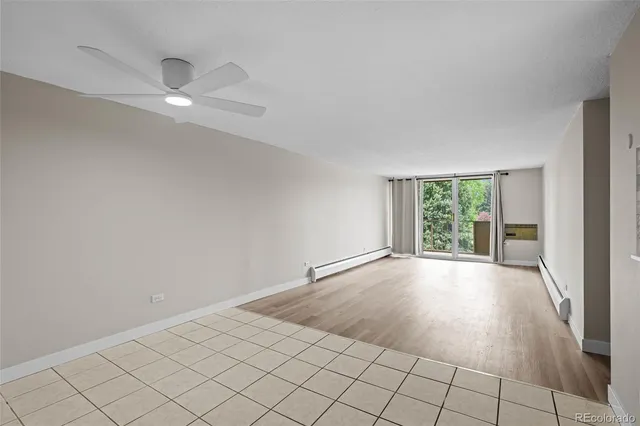 a view of an empty room with wooden floor and a kitchen