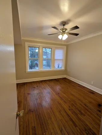 an empty room with wooden floor chandelier fan and windows