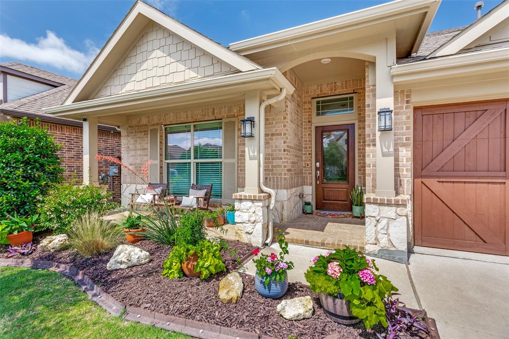 5556 Vaquero Road Fort Worth, TX 76126 - Photo 3 of 25 Brick and stone veneer exterior featuring a covered porch, wood-paneled garage door, and a professionally landscaped front bed with mulch