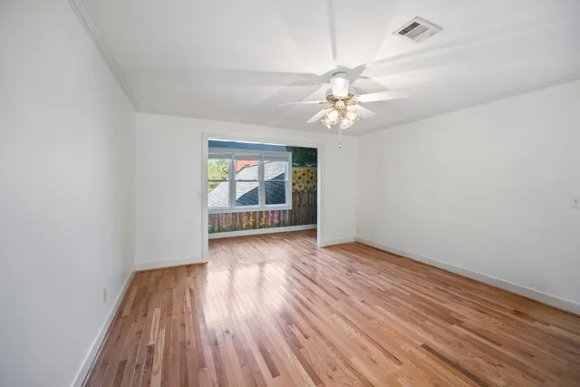 an empty room with wooden floor chandelier fan and windows