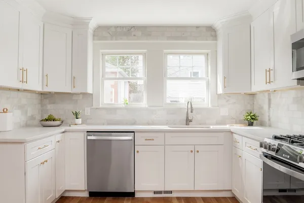a kitchen with white cabinets appliances a sink and a window
