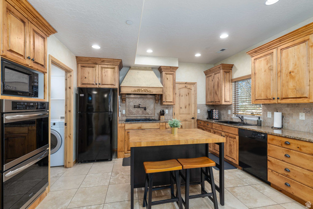 5168 Fairview Loop, Unit C604 Eden, UT 84310 - Photo 4 of 53 Kitchen with black appliances, light stone countertops, washer / clothes dryer, decorative backsplash, and light tile patterned flooring