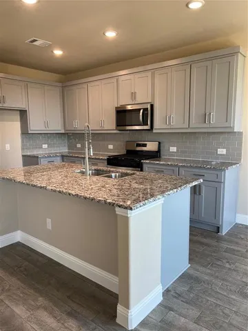 a kitchen with granite countertop a sink a stove a microwave a counter top space and cabinets