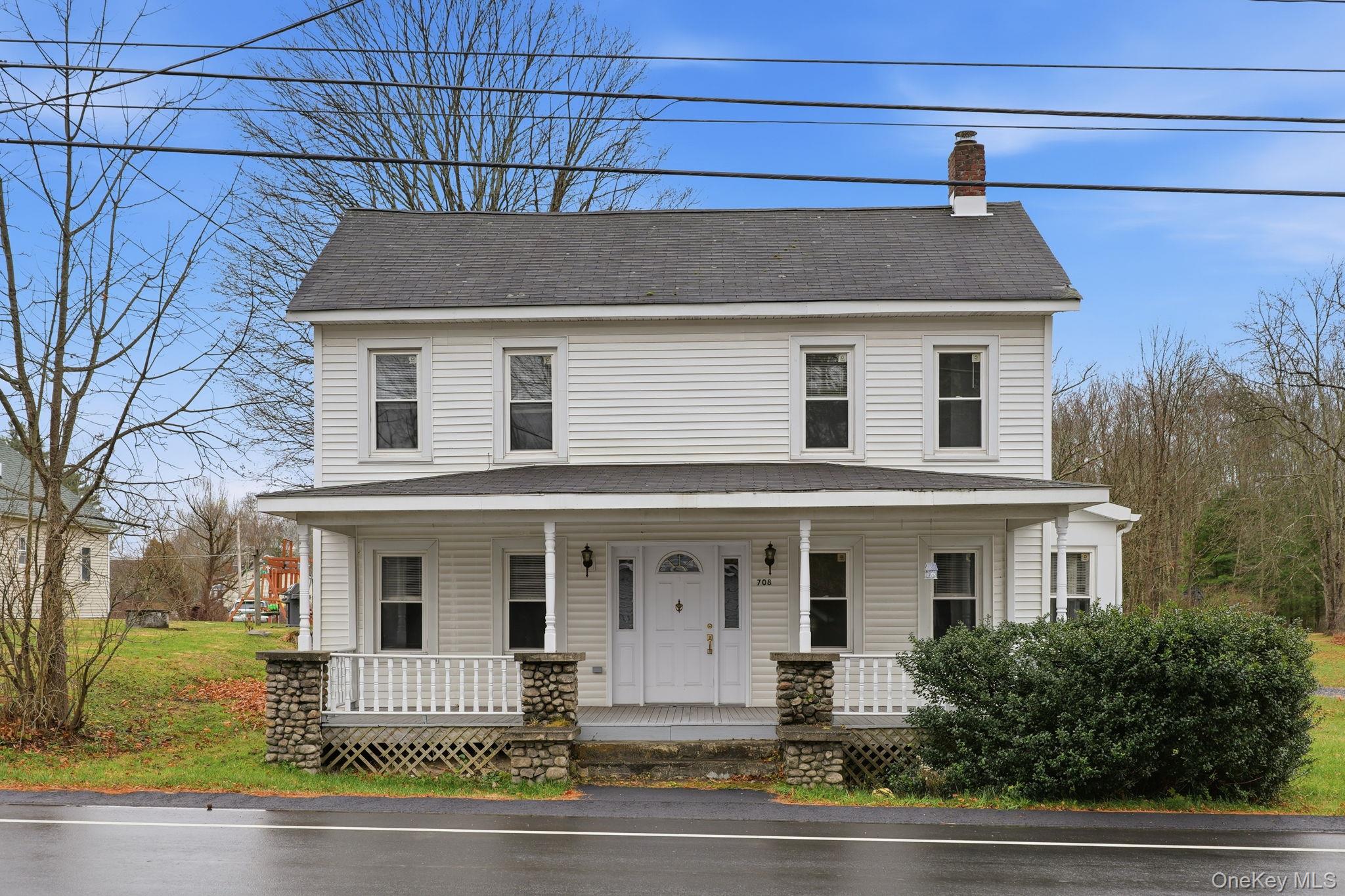 View of front facade featuring covered porch, a chimney, a shingled roof, and a front lawn