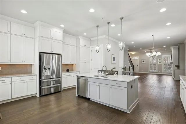 a kitchen with stainless steel appliances kitchen island a refrigerator oven a sink a stove and white cabinets with wooden floor