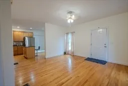 a view of an empty room and kitchen with wooden floor