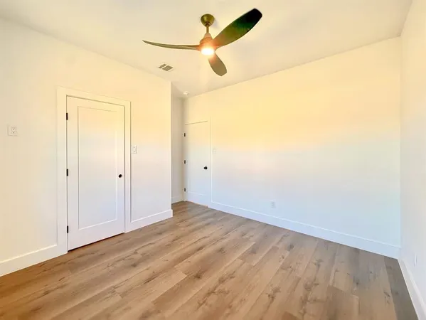 an empty room with wooden floor ceiling fan and window