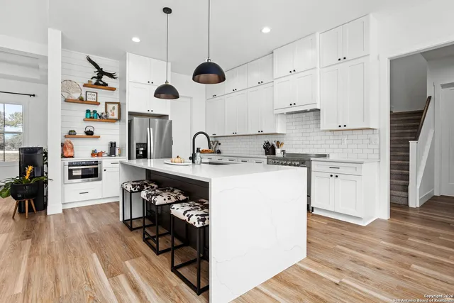 a kitchen with stainless steel appliances kitchen island granite countertop a sink a stove and a wooden floors