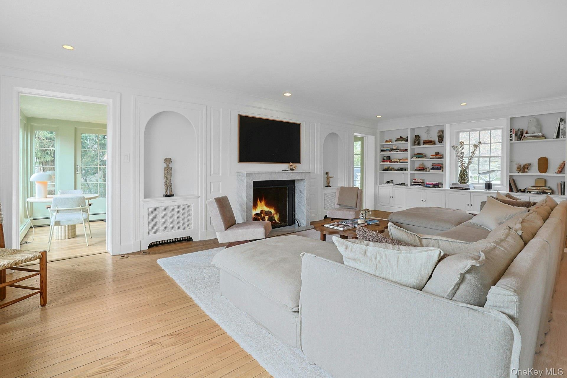 21 Tisdale Road Scarsdale, NY 10583 - Photo 3 of 40 Expansive, light-filled living room anchored by a gas fireplace, with custom built-ins and bay window framing a tranquil Crane Berkley pond view and a seamless connection to the sunroom. Ideal for relaxing and hosting.
