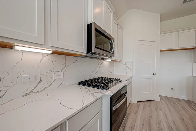 a kitchen with white cabinets a sink stove and microwave