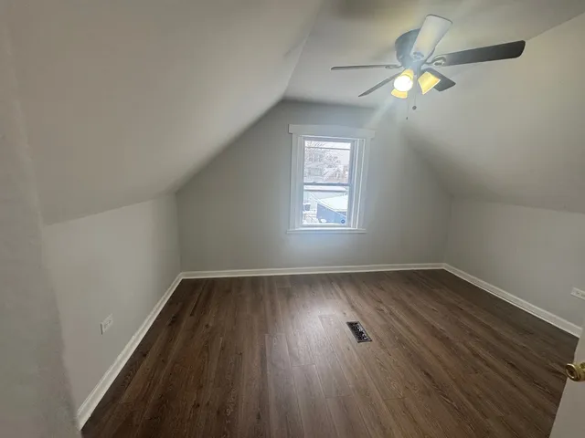an empty room with wooden floor chandelier fan and windows