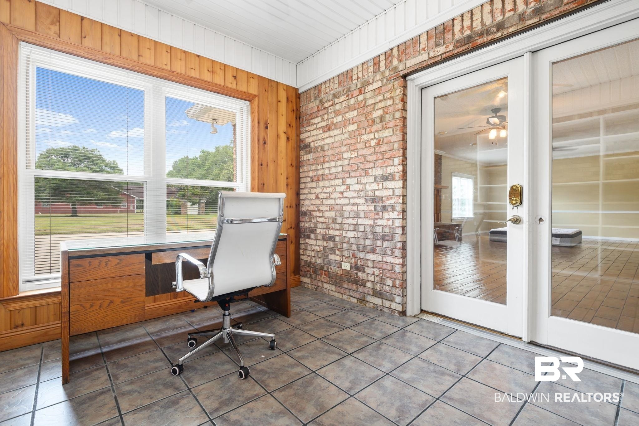7540 2 Mile Road Irvington, AL 36544 - Photo 42 of 82 Bright room featuring a large window, tiled flooring, wood paneling, exposed brick wall, and glass French doors