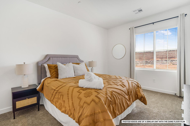 1702 Ripple Rock Drive, Unit 3171 Washington, UT 84780 - Photo 14 of 16 Bedroom with an upholstered headboard, carpet flooring, a window with horizontal blinds, and a circular wall mirror