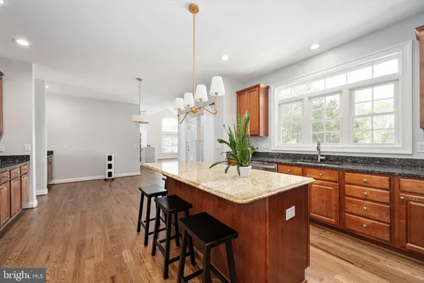 a kitchen with stainless steel appliances granite countertop wooden cabinets a stove a sink a refrigerator and island with wooden floor