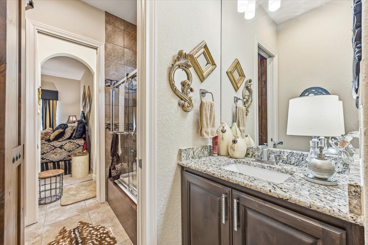 1930 Rothschild New Braunfels, TX 78132 - Photo 18 of 39 The bathroom features a vanity with a granite countertop and a square sink, a shower with sliding glass doors and tiled walls, and tiled flooring