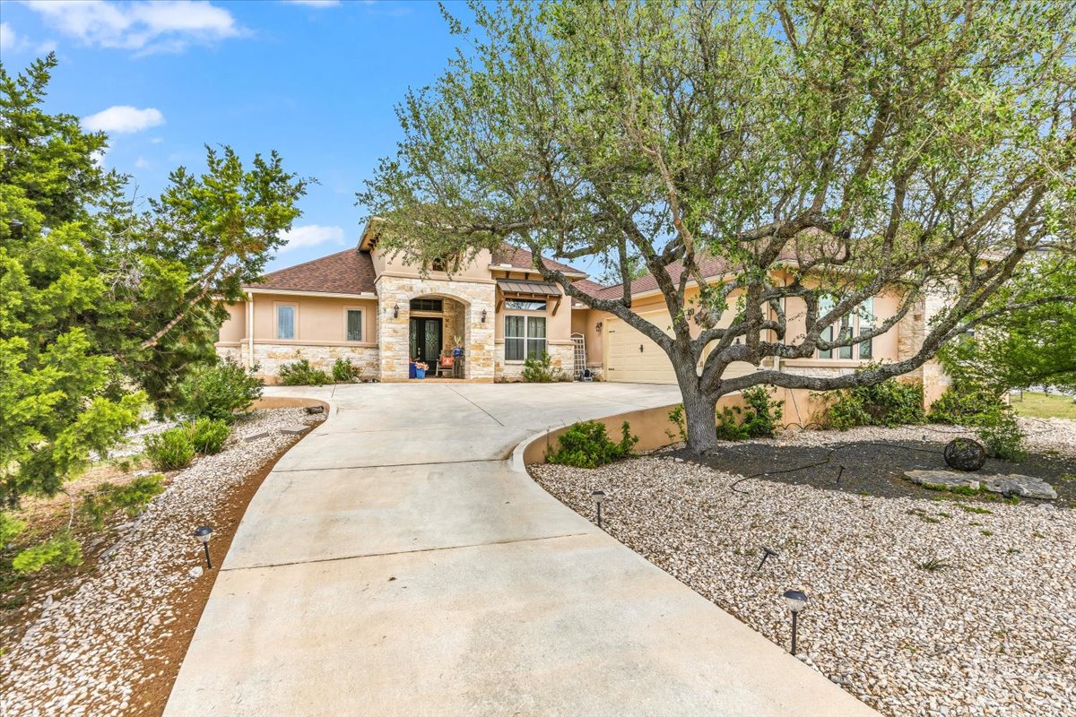 1930 Rothschild New Braunfels, TX 78132 - Photo 2 of 39 The property features an inviting concrete driveway, a stone and stucco exterior, and a prominent mature tree with extensive branches