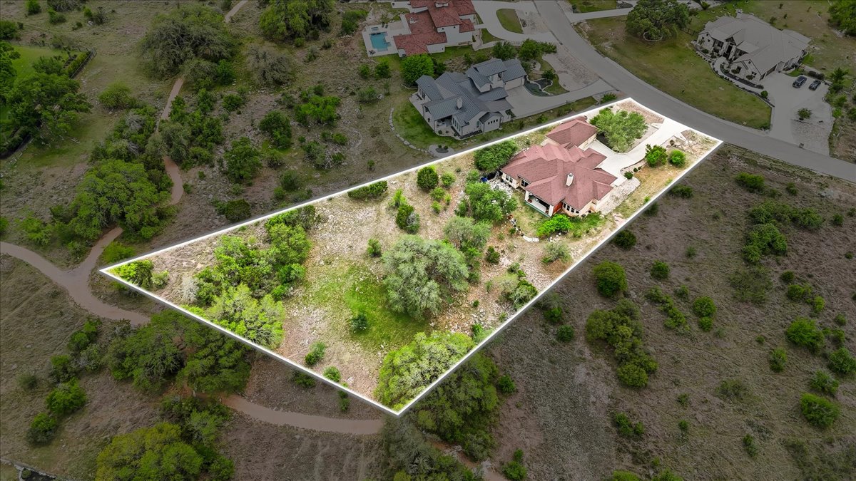 1930 Rothschild New Braunfels, TX 78132 - Photo 4 of 39 Aerial view showcasing the property's expansive grounds, featuring a residence with a red-tiled roof and a paved driveway, surrounded by natural vegetation