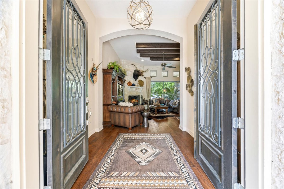 1930 Rothschild New Braunfels, TX 78132 - Photo 6 of 39 The property features a grand entrance with ornate double doors, leading into a living area with hardwood floors, exposed ceiling beams, and a stone fireplace
