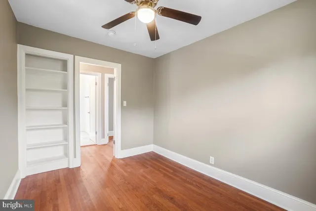 an empty room with wooden floor chandelier fan and windows